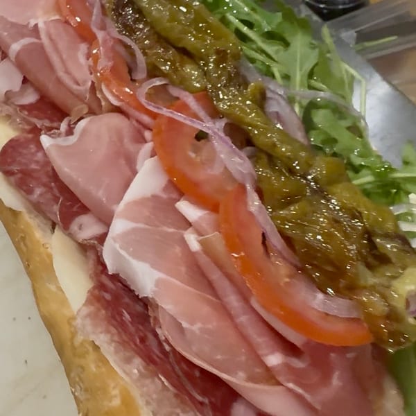 Close-up of a large Italian sub sandwich with various meats, cheese, tomatoes, onions, and peppers.