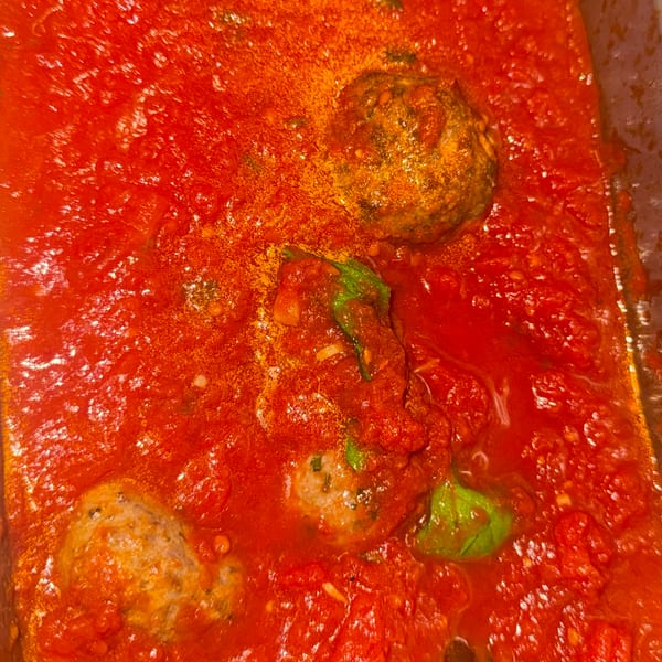 Meatballs simmering in a rich red tomato sauce with fresh basil leaves and a serving spoon.