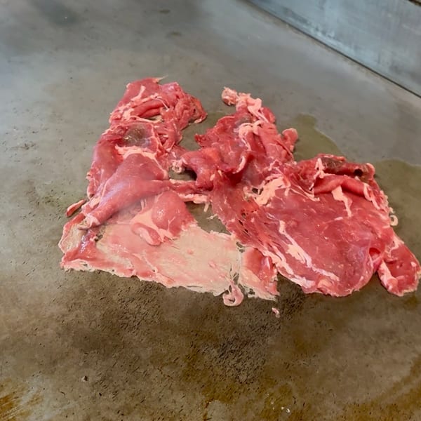 Thinly sliced raw beef cooking on a flat-top grill, with some fat rendering.