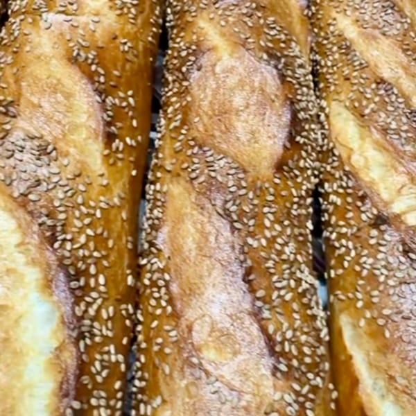 Close-up of golden-brown baguettes, generously sprinkled with sesame seeds, fresh from the oven.