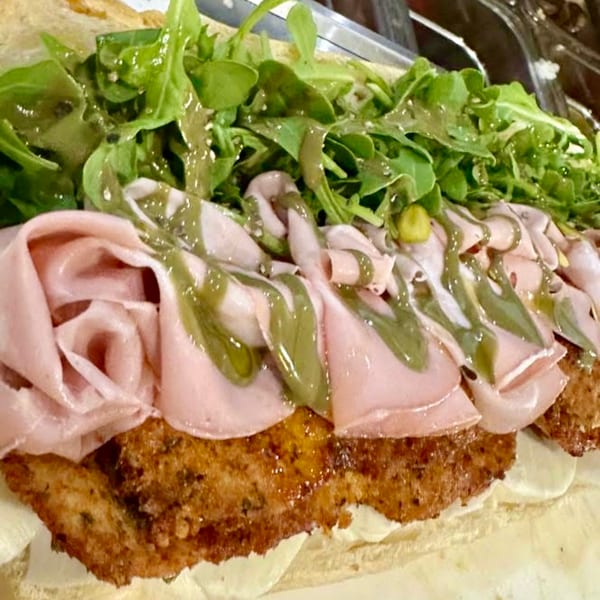 Close-up of a sandwich with fried chicken cutlet, mortadella, arugula, and green dressing.